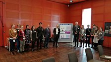 Eine Gruppe von 15 Personen steht neben einer Plakatstellwand