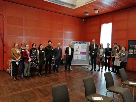 Eine Gruppe von 15 Personen steht neben einer Plakatstellwand