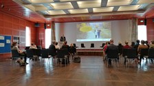 Personen sitzen in einem Saal, vorn steht ein Redner