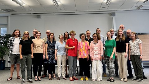 Gruppenfoto des Treffens, es sind 19 Personen vor einer Leinwand zu sehen