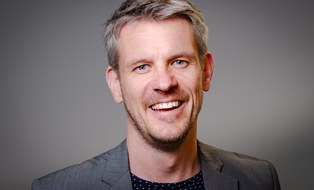 white male with grey jacket smiles into the camera