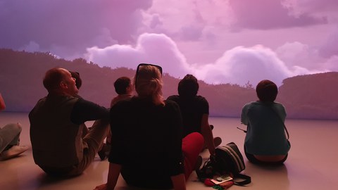 Personen sitzen vor einer bunten Wand mit dem Rücken zum Fotografen