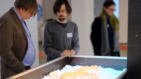 Eine Person erklärt einer anderen an einem Sandkasten