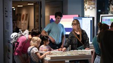 Foto von 2 Kindern und mehreren erwachsenen Personen an einem interaktiven Ausstellungsmodul im COSMO Wissenschaftsforum