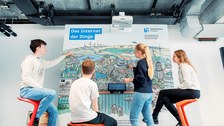 Foto von 4 Jugendliche,, die an einer am Stadtbild von Dresden inspirierten, interaktiven Stadtansicht mit der Überschrift "Das Internet der Dinge" die Funktionen ausprobieren.