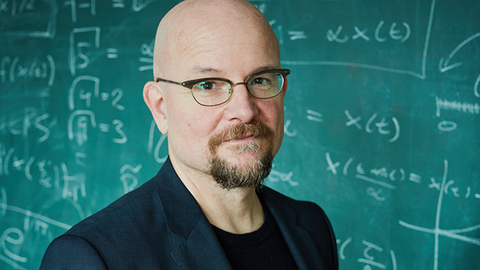 Foto von Prof. Dirk Brockmann vor einer Tafel mit Formeln.