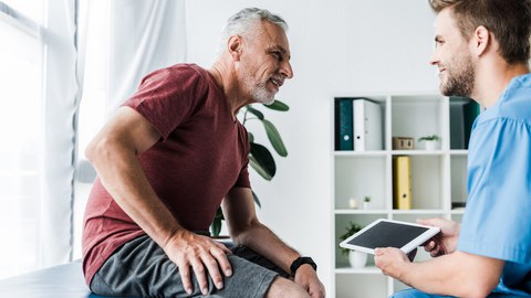 Picture of two people. One person is sitting on a doctor's couch and talking to a doctor.