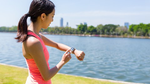 Photo of a young woman by a river starting her smartwatch for running training