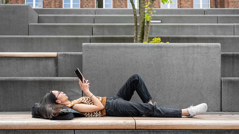 A university student lying on a staircase while scrolling through content on a tablet.
