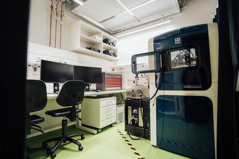 A room with a device with open door and two chairs in front of a desk with two screens.