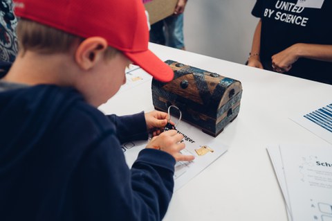 A photo of a child opening the lock of a treasure chest.