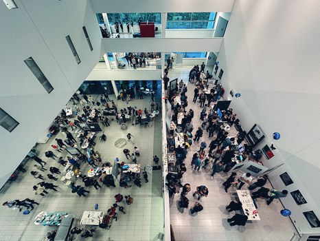 A top down photo of a hall with several floors, filled with visitors and exhibition booths.