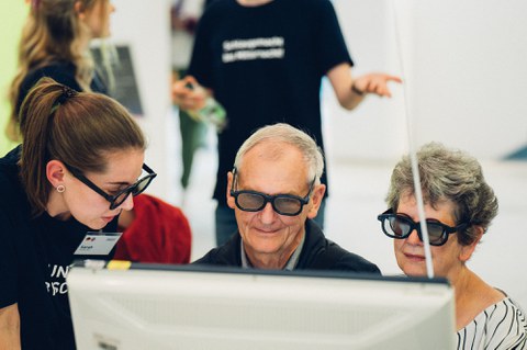 A photo of three people who are looking at a screen while wearing special glasses.