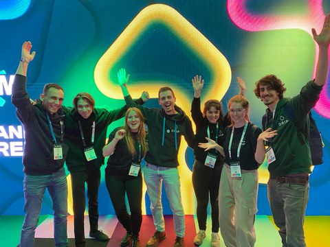 A group photo. 7 people in front of a digital screen posing happily.