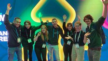 A group photo. 7 people in front of a digital screen posing happily.