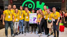 A group photo. 11 young people pose together. All are wearing the same yellow t-shirts. The person in the middle holds a poster that says "WunderBand"