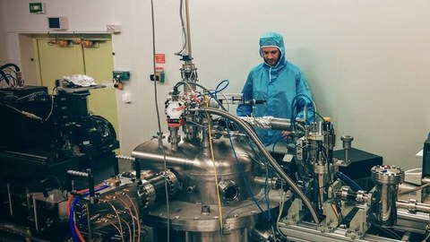 A man in protective clothing stands behind a complex machine