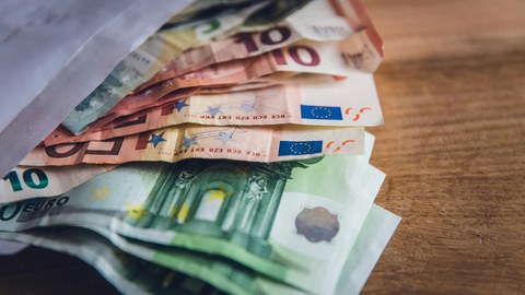 Ein Foto. Auf dem Tisch liegen Euro-Banknoten, die teilweise aus einem weißen Umschlag entnommen wurden.
