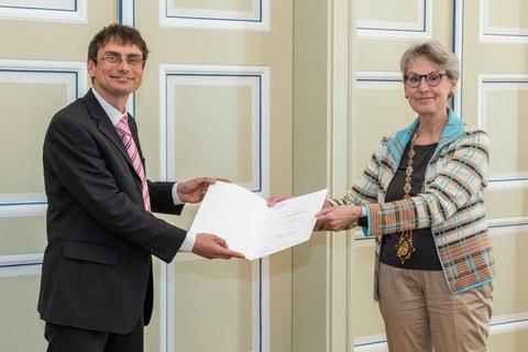 Ein Mann auf der linken Seite erhält ein Diplom von der Frau auf der rechten Seite. Beide lächeln