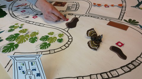 Papier mit darauf gemaltem Spielfeld und Objekte zum Beispiel einer Eingangstür Hand die eine Spielfigur auf dem Feld bewegt