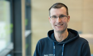Foto: Mann mit kurzen grau-schwarzen Haaren und Brille, im dunkelblauen Kapuzenpullover mit DHSZ-Logo