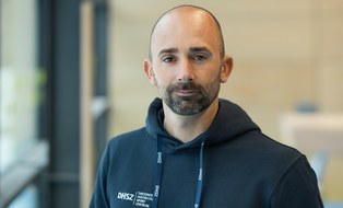 Foto: Mann mit sehr kurzen schwarzen Haaren, im dunkelblauen Kapuzenpullover mit DHSZ-Logo