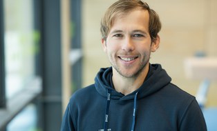 Foto: Mann mit kurzen blonden Haaren, im dunkelblauen Kapuzenpullover mit DHSZ-Logo