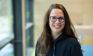 Foto: junge Frau mit langen rotbraunen Haaren und Brille, im dunkelblauen Kapuzenpullover mit DHSZ-Logo