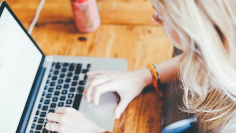 Foto: Schreibtisch mit aufgeklapptem Laptop und daran arbeitendem Menschen