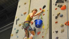 Eine Kursleiterin an der Kletterwand zeigt das Victoryzeichen