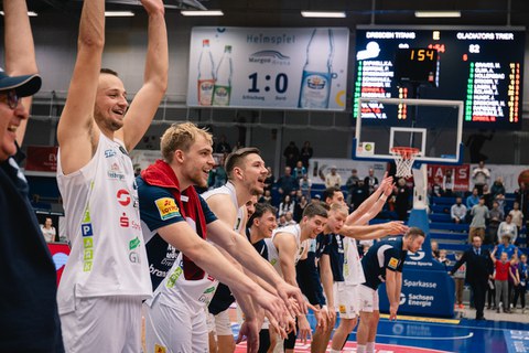 Foto: junge Sportler mit erhobenen Armen im weißen und blauen Trikots (Auffoerung zur La-Ola-Welle)