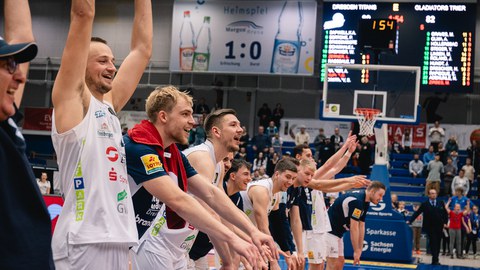 Foto: junge Sportler mit erhobenen Armen im weißen und blauen Trikots (Auffoerung zur La-Ola-Welle)