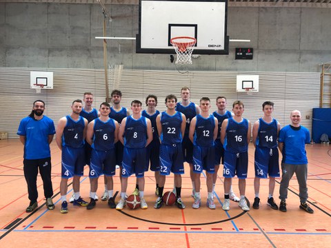 Foto Gruppe junger Männer in Sportkleidung als Mannschaft aufgestellt vor einem Basketballkorb