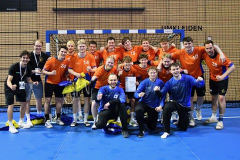 Foto: eine männliche Mannschaft in orangenen Shirt in Jubelpose vor einem Tor