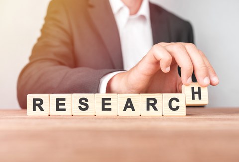 Mann baut das Wort "RESEARCH" aus Holztäfelchen vor sich auf.
