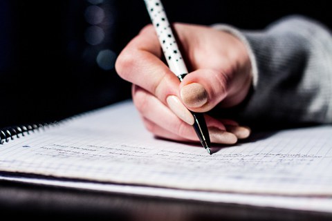 Hand holding a pen and writing on sheet of paper