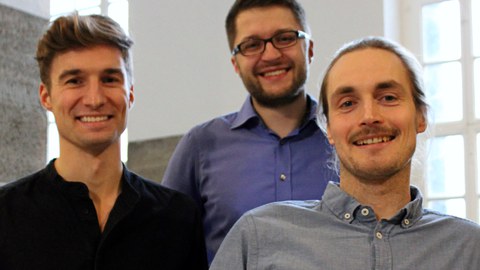 Foto: drei Männer ´stehen nah beieinander und blicken in die Kamera
