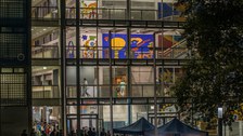 Foto des Hörsaalzentrums der TU Dresden am Abend mit Blick ins Innere. Es sind bunte Wände zu sehen und viele Personen vor dem Gebäude. 