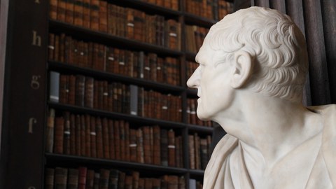 Statue zu Büchern im Hintergrund blickend