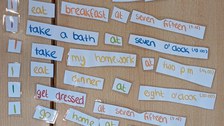Vogelperspektive: Auf einem Tisch liegen englische Wortkarten in verschiedenen Farben. Eine Schülerin schreibt in ihr Heft.