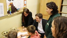 Zwei Schüler experimentieren zwei Schüler mit eienr alten Waage und Gewichten. Vier Erwachsene schauen ihnen über die Schulter und unterstützen.