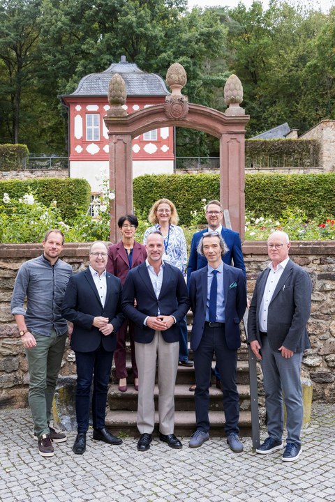 Gruppenfoto von acht Personen vor einem steinerne Torbogen und einem historischen rot-weißen Gebäude im Hintergrund. Im Vordergrund stehen Sebastian Macho, Markus Harzenetter, Julius Wagner, Mirko Breitenstein und Ingo Schon, dahinter auf den Stufen Doris Moos, Gaby Lindenmann-Merz und Christoph Degen.