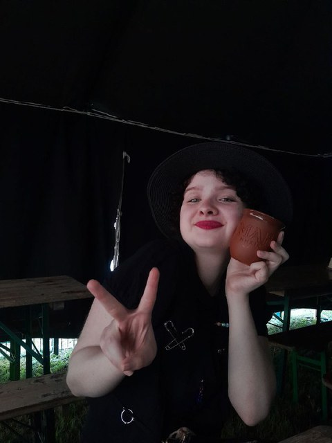 Porträt von Josy auf dem sie sich einen Becher an die Wange hält und mit der anderen Hand das Peace Zeichen macht.