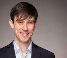 Ein lächelnder Mann im Anzug vor einem grauen Hintergrund