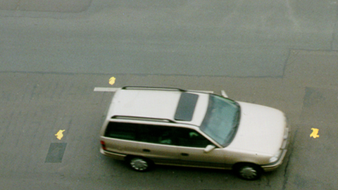 A lone white car on an asphalt road, seen from a bird's-eye view.