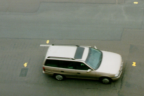 A lone white car on an asphalt road, seen from a bird's-eye view.