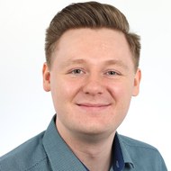 Jean Coert ist ein junger, weißer Mann mit blonden Haaren. Sein Portrait zeigt ihnfreundlich lächelnd vor einem weißen Hintergrund. Er trägt ein blaugrünes Hemd.