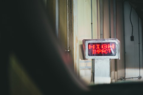 Ein alter Korridor in dem ein Monitor steht, auf dem in rot leuchtender, Pixelschrift "High Impact" zu lesen ist.