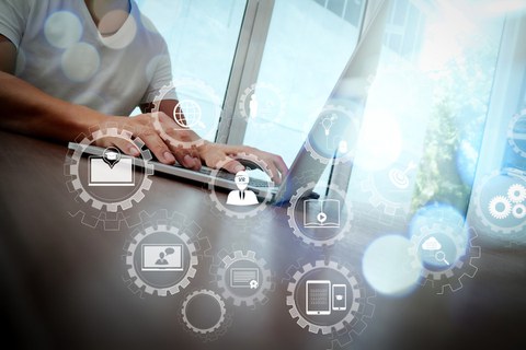 Photo: A man is sitting at a table at the laptop. In the foreground are symbols that stand for technology and studies.
