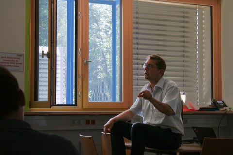 Prof. Christian Prunitsch sitzt auf einem Tisch und gestikuliert